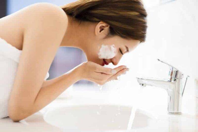 young woman washing face with clean water in bathroom