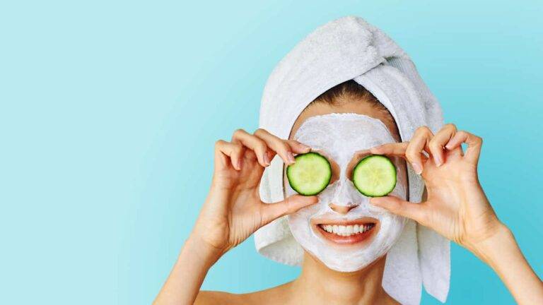 beautiful young woman with facial mask on her face holding slices of cucumber