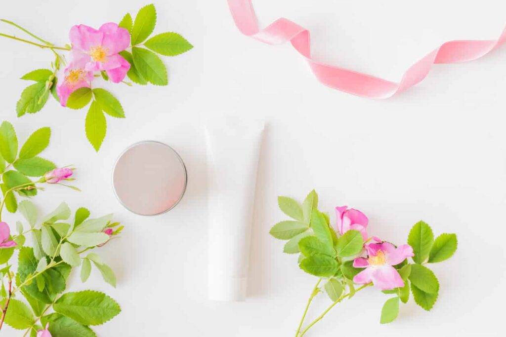 flat lay composition with cosmetic products, mockup white tubes and pink flower on a white background